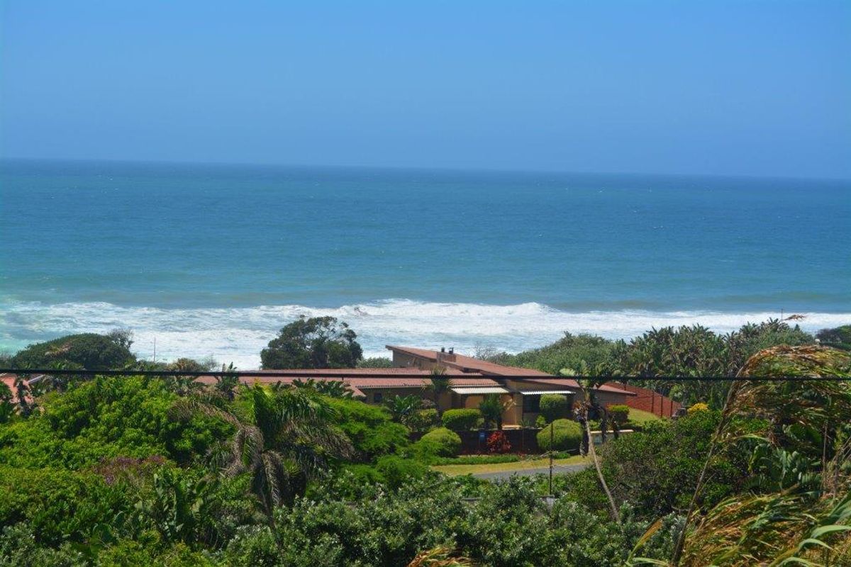 Elevated aerial view of a coastal property featuring a low-pitched roofline, surrounded by lush greenery with direct ocean views.