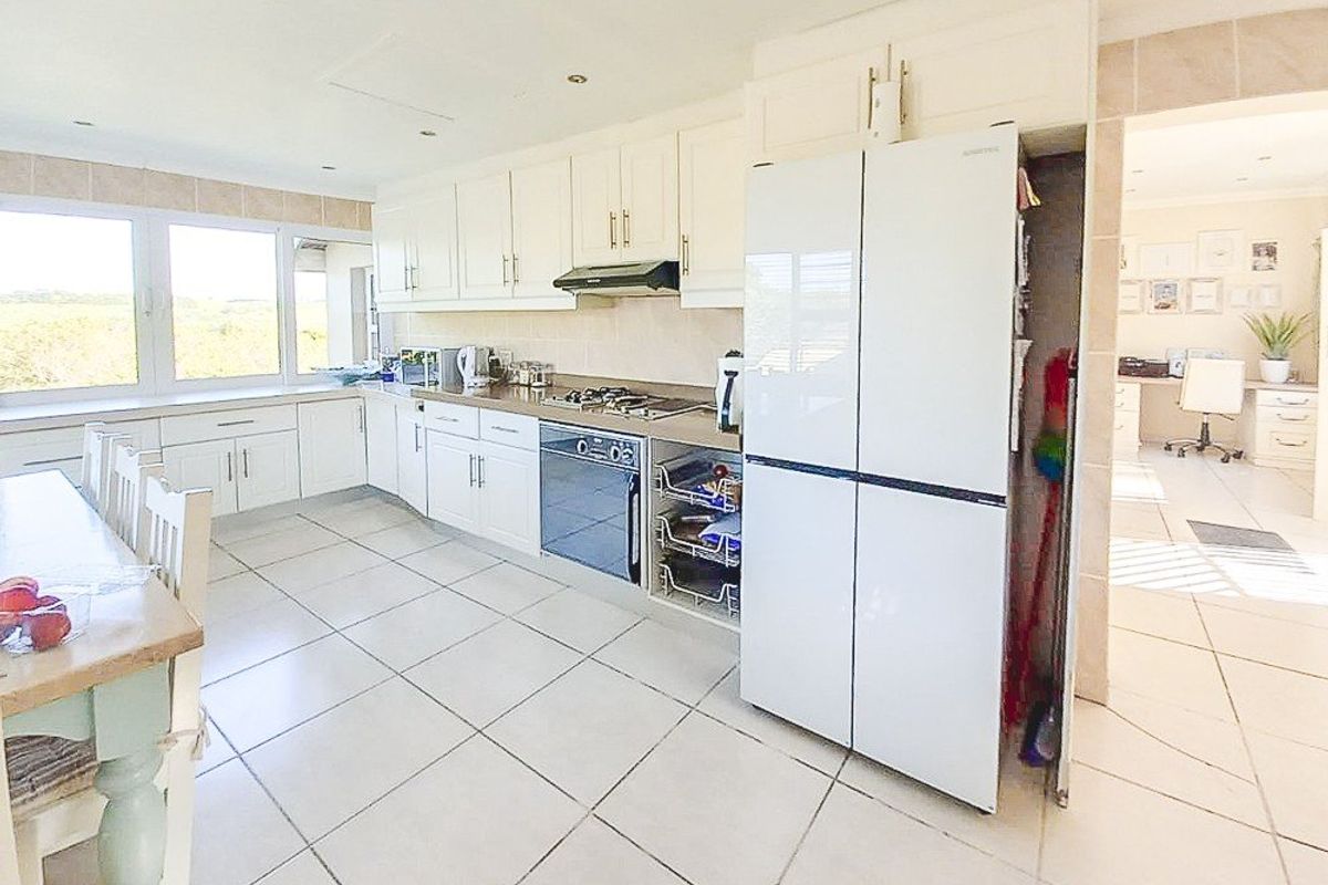 A bright, functional kitchen featuring white cabinetry, tiled flooring, built-in oven and hob, and ample natural light from large windows.