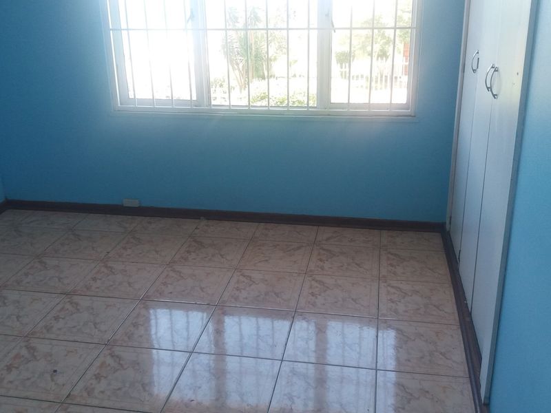 An empty bedroom featuring tiled flooring, built-in cupboards, and a window fitted with security bars.