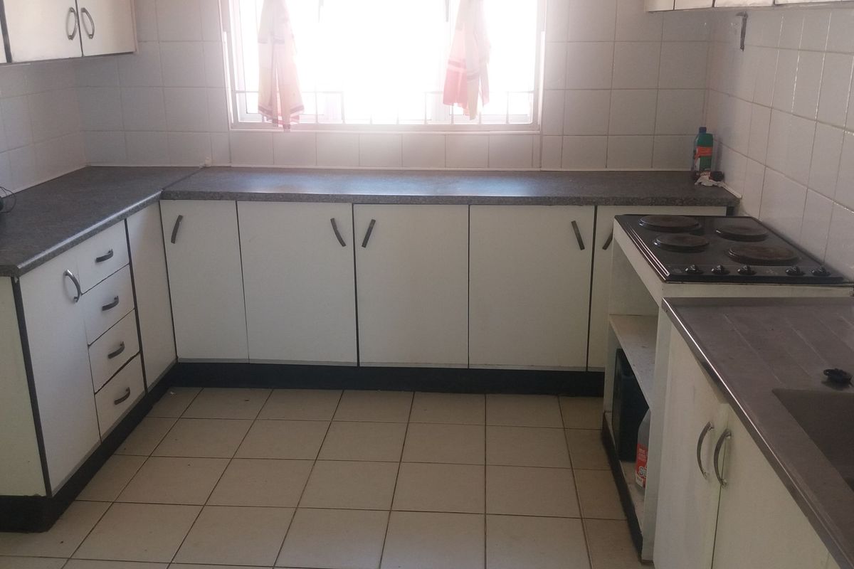 A functional kitchen featuring white cabinetry, laminate countertops, an integrated electric hob, and a stainless steel sink with tiled splashbacks.