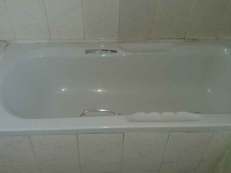 A standard built-in bathtub with chrome fixtures and tiled surround, showing signs of age and wear in the grout and tile finishes.