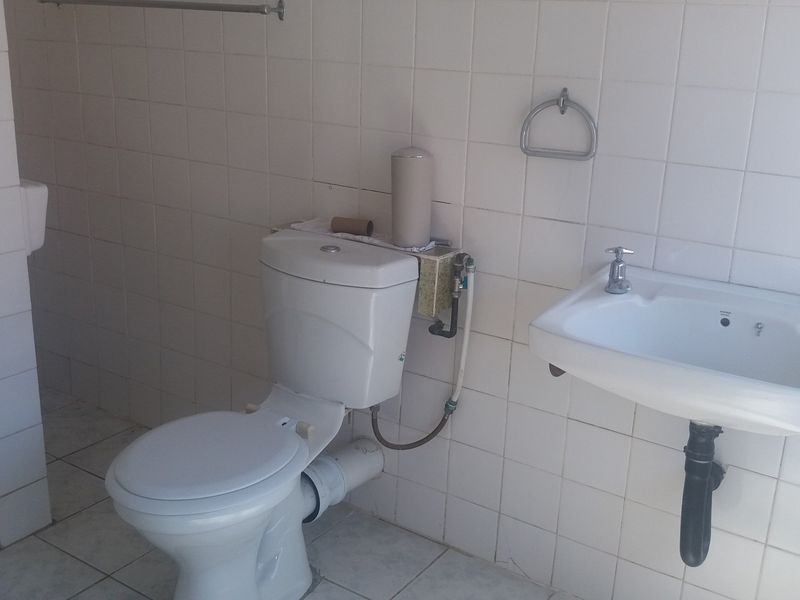 A functional bathroom featuring a wall-mounted basin, toilet, and shower enclosure with fully tiled walls and flooring.