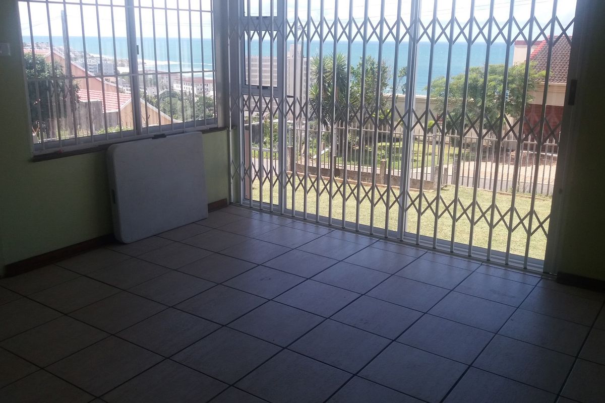 An empty living area featuring tiled flooring, security gates, and large sliding doors that offer expansive views of the ocean.