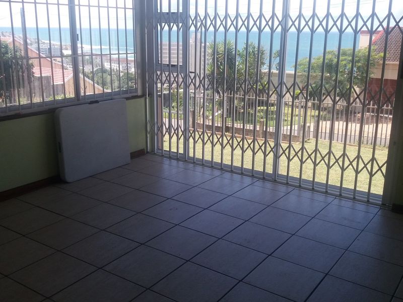 An empty living area featuring tiled flooring, security gates, and large sliding doors that offer expansive views of the ocean.