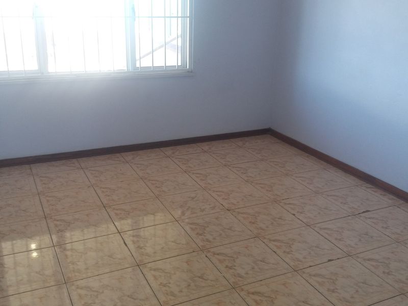 An empty bedroom featuring tiled flooring, skirting boards, and a window fitted with security bars.