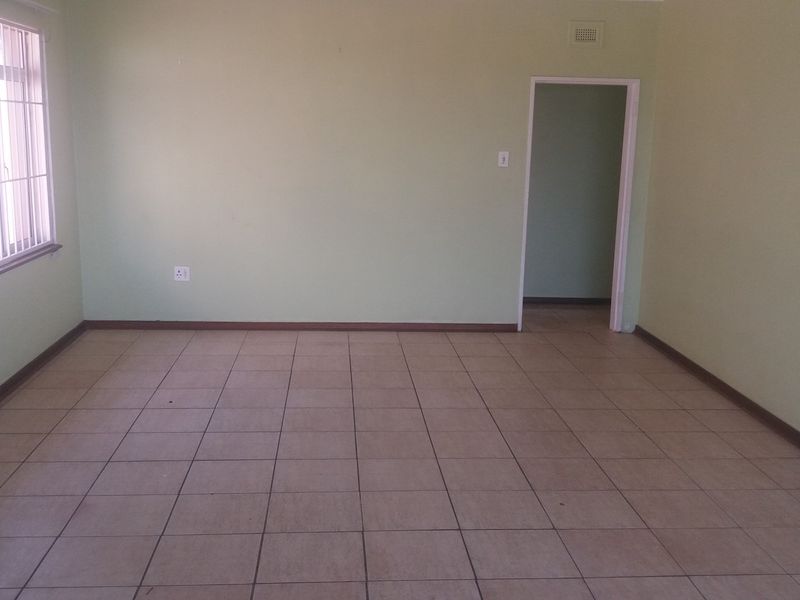 An empty living room featuring neutral wall paint, tiled flooring, and a window fitted with security bars.