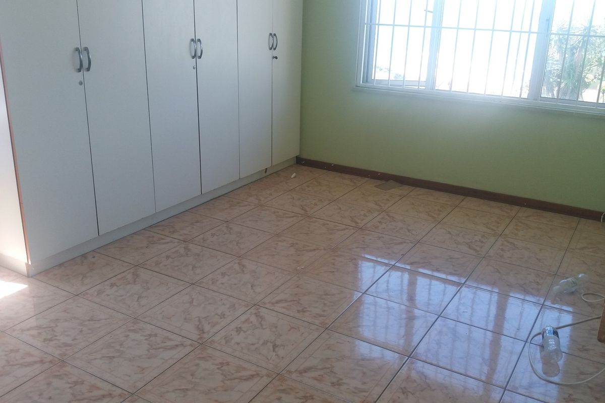 A vacant bedroom featuring built-in cupboards, tiled flooring, and a window fitted with security bars.