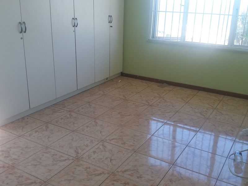 A vacant bedroom featuring built-in cupboards, tiled flooring, and a window fitted with security bars.