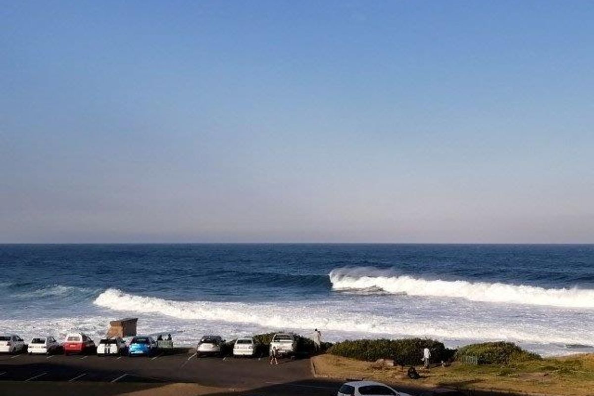 A scenic coastal view overlooking the ocean with breaking waves and a parking area in the foreground.