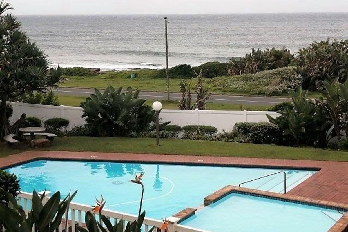 Outdoor pool and spa area featuring brick paving, landscaped garden, and white perimeter fencing with scenic ocean views.