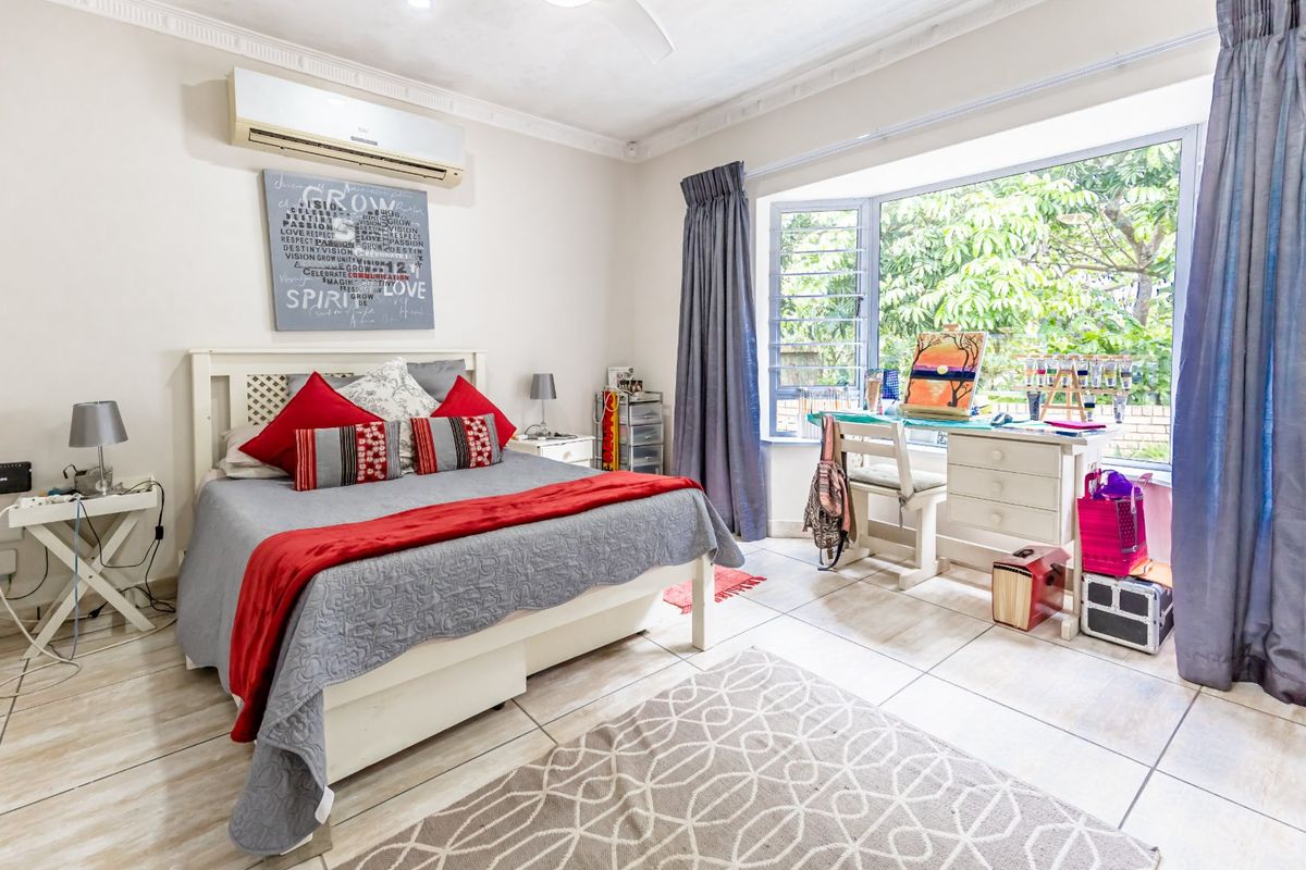 A well-lit bedroom featuring tiled flooring, a large bay window, and a wall-mounted air conditioning unit.