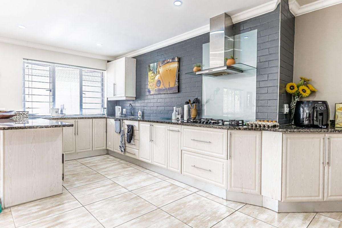 Modern kitchen featuring light wood cabinetry, granite countertops, a gas hob with stainless steel extractor fan, and a striking grey brick feature wall.