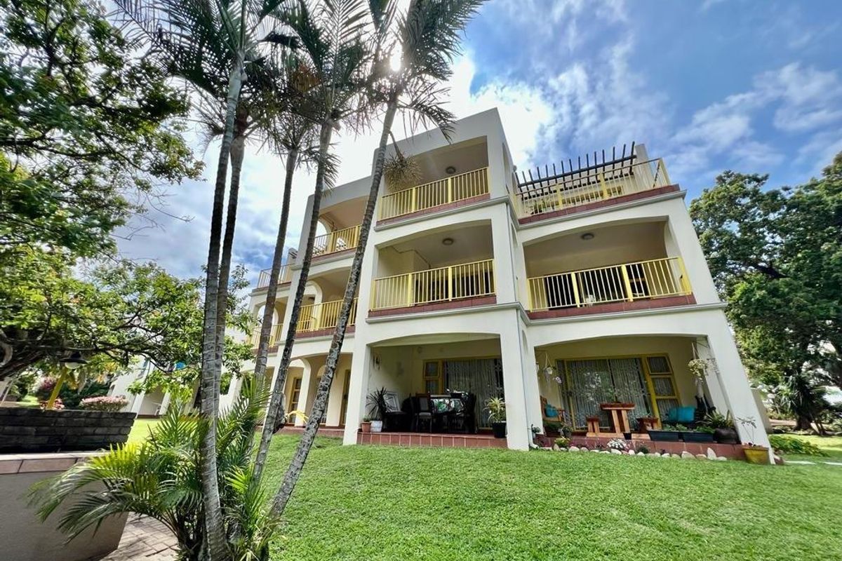Rear elevation of a multi-story apartment building featuring stacked balconies with metal railings, sliding glass doors, and a ground-floor patio overlooking a garden.