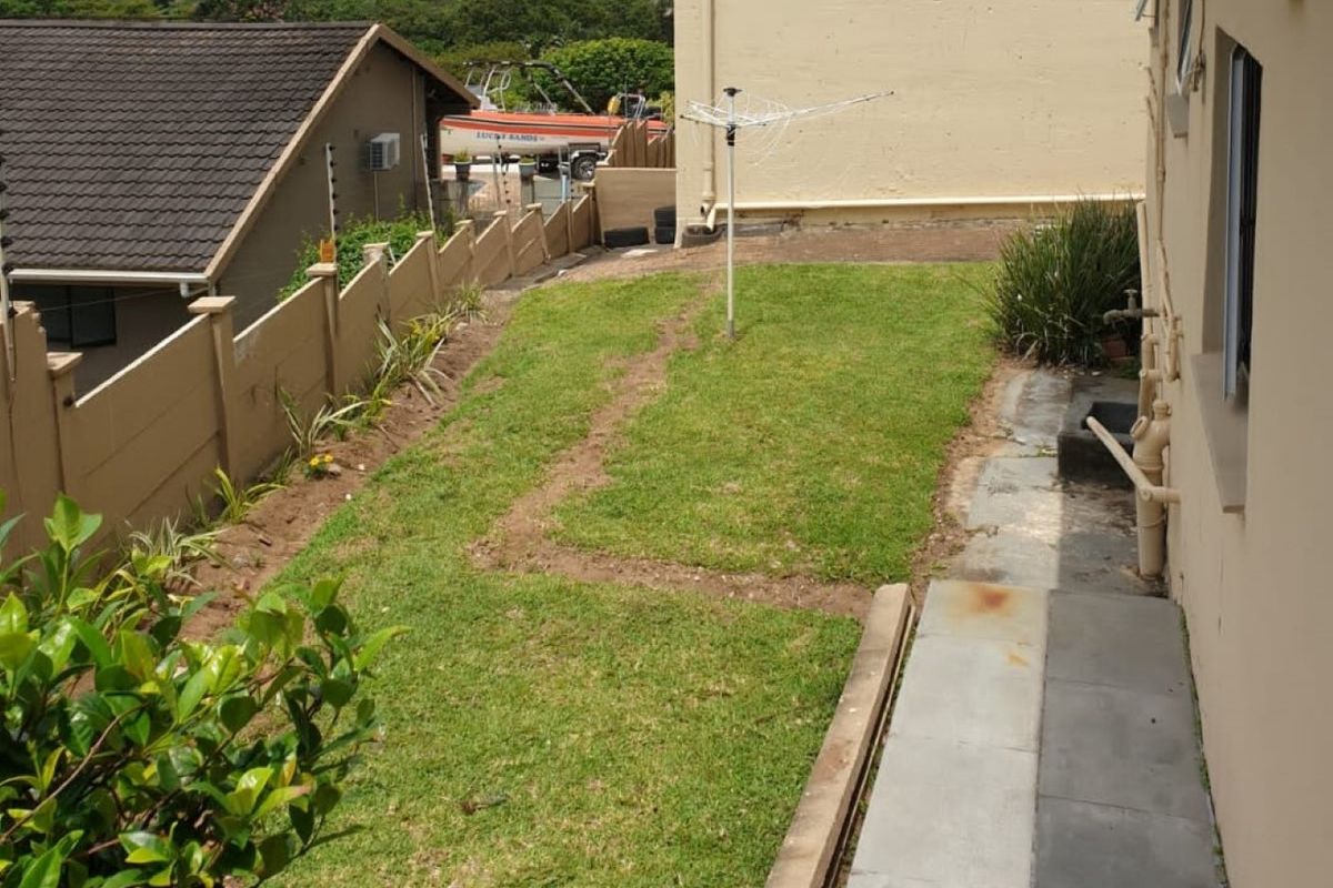 Rear garden area featuring a lawn, precast boundary wall, and paved walkway along the side of the townhouse.