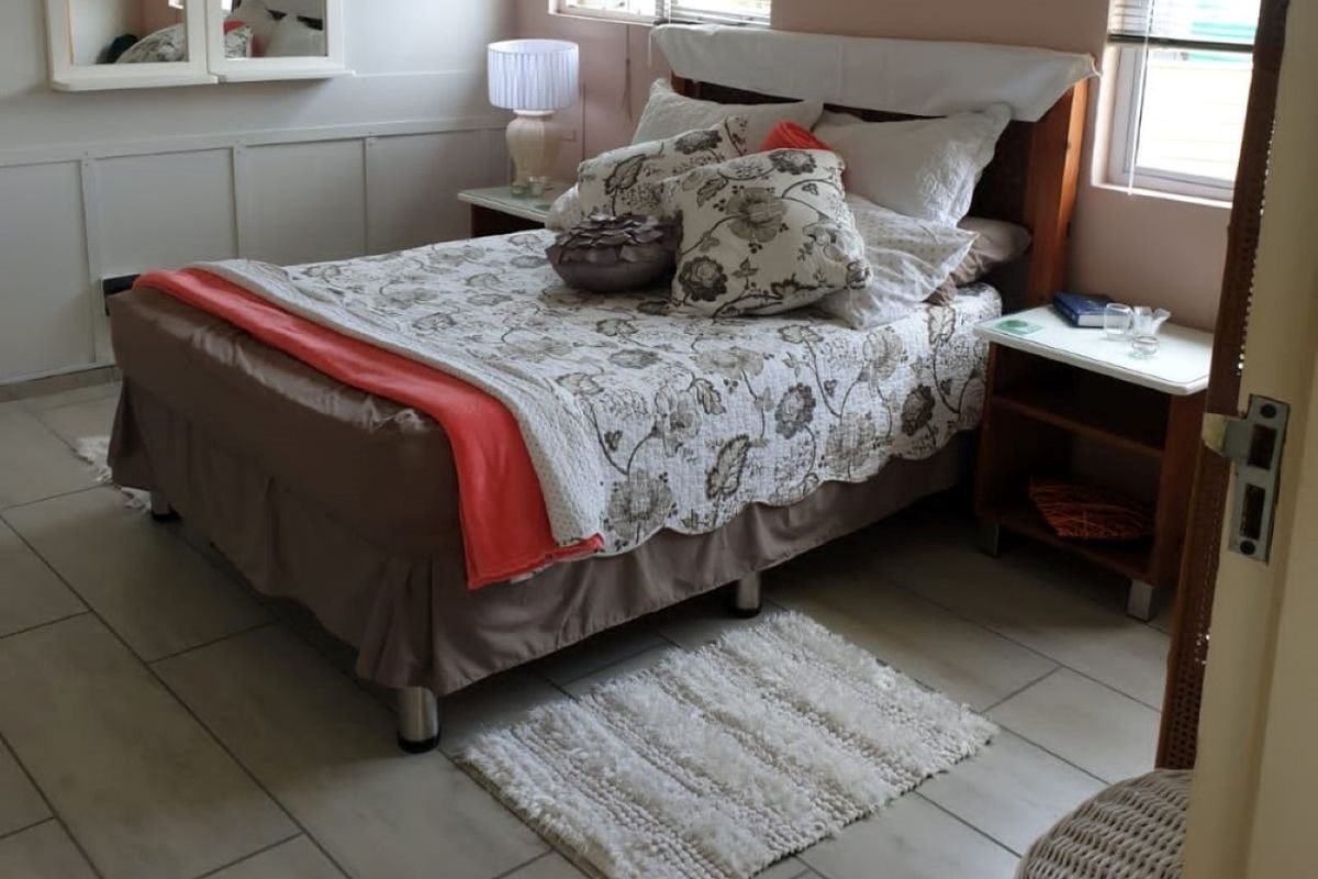 A bedroom featuring tiled flooring, wall paneling, and a built-in mirror, offering a functional space with natural light from the windows.