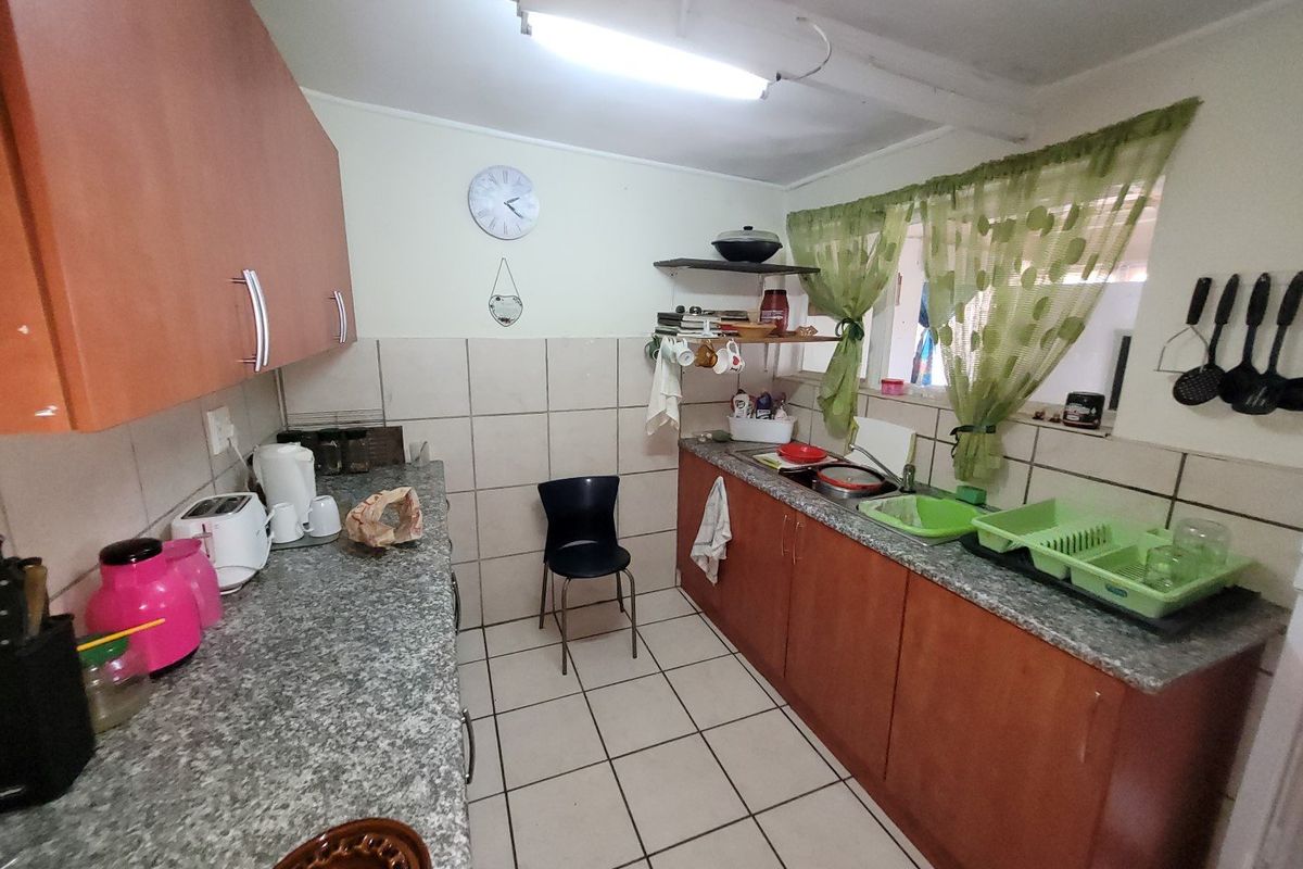 A functional kitchen featuring laminate cabinetry, granite-look countertops, and tiled flooring, offering a practical layout with potential for modern cosmetic updates.