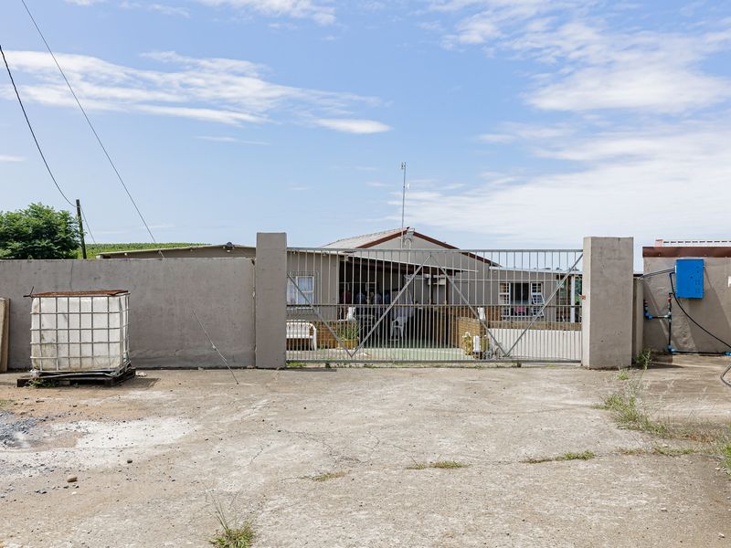 Front view of an industrial property featuring a concrete driveway, secure metal gate, and perimeter walling with external utility connections.