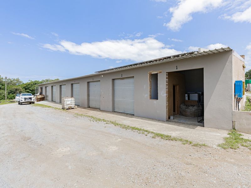 Industrial storage facility featuring multiple roller shutter doors, a corrugated metal roof, and an unfinished entrance bay requiring completion.