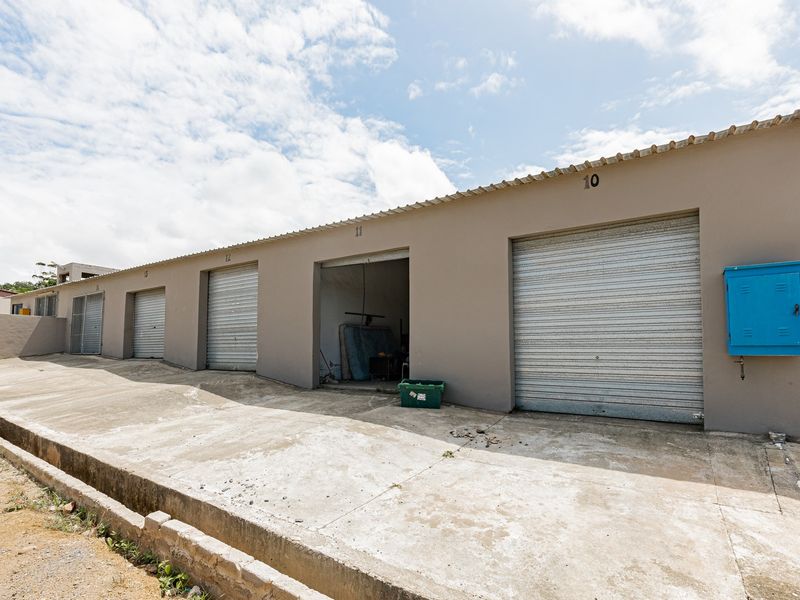 A row of industrial storage units featuring roller shutter doors and a concrete driveway area.