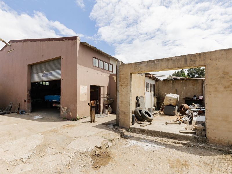 Rear exterior view of an industrial property featuring a large roller shutter door, concrete yard area, and an open-sided masonry storage structure.