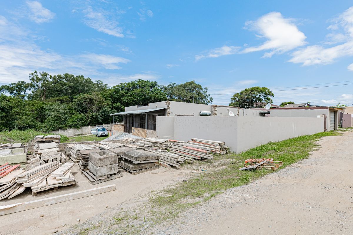 Rear exterior view of the industrial property featuring a perimeter wall, security bars, and an unpaved yard area with construction materials.