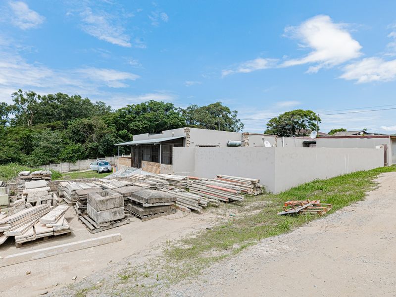 Rear exterior view of the industrial property featuring a perimeter wall, security bars, and an unpaved yard area with construction materials.