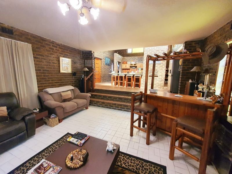 Open plan living area featuring exposed brick walls, tiled flooring, a raised platform leading to the kitchen, and a built-in bar area.