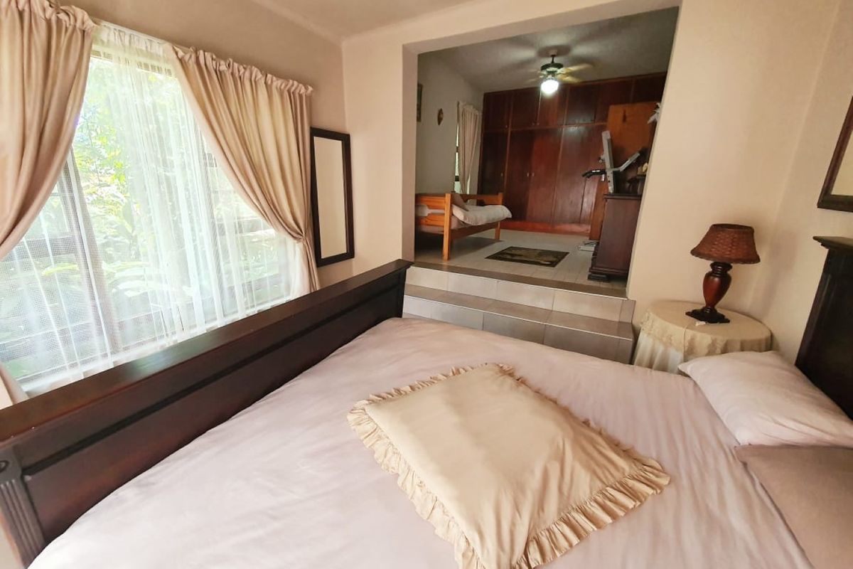 Spacious bedroom featuring a raised platform area with built-in wooden cupboards and a ceiling fan, offering a versatile layout.