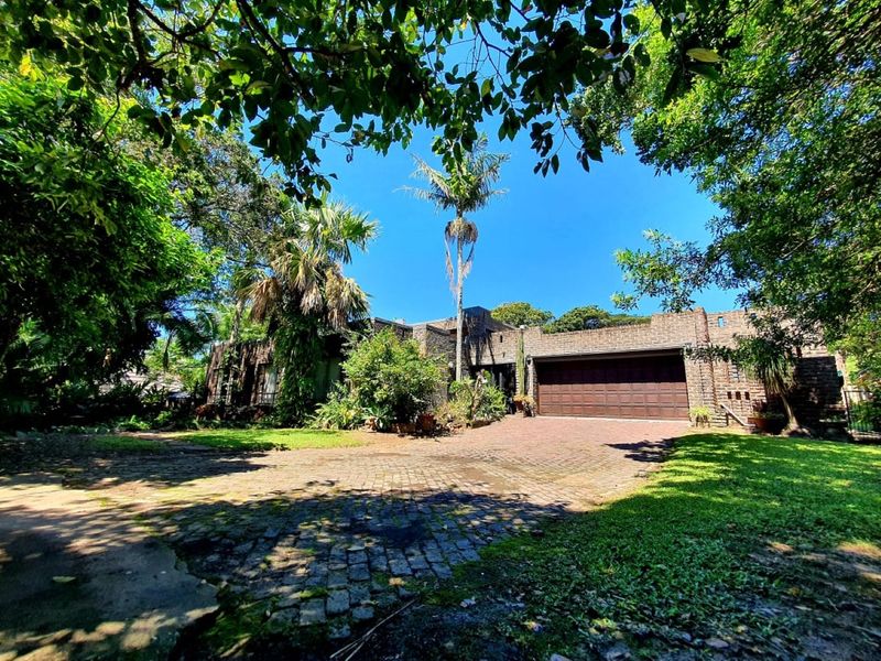 Front view of a brick-faced house featuring a paved driveway, double garage, and established garden with mature trees.