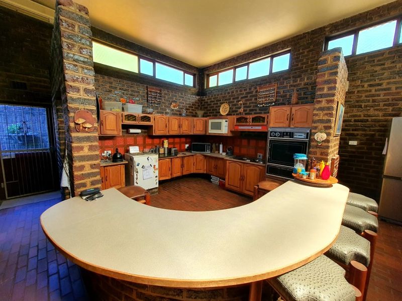 Spacious kitchen featuring exposed brick walls, custom wooden cabinetry, a curved breakfast bar, and built-in appliances, offering a unique rustic aesthetic.