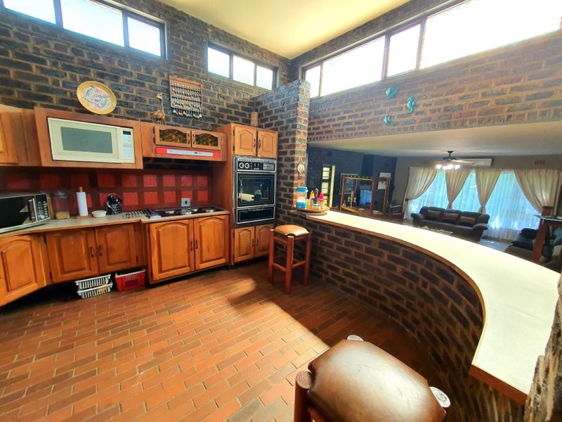 Open-plan kitchen and living area featuring exposed brick walls, terracotta flooring, built-in wooden cabinetry, and a breakfast bar with clerestory windows.
