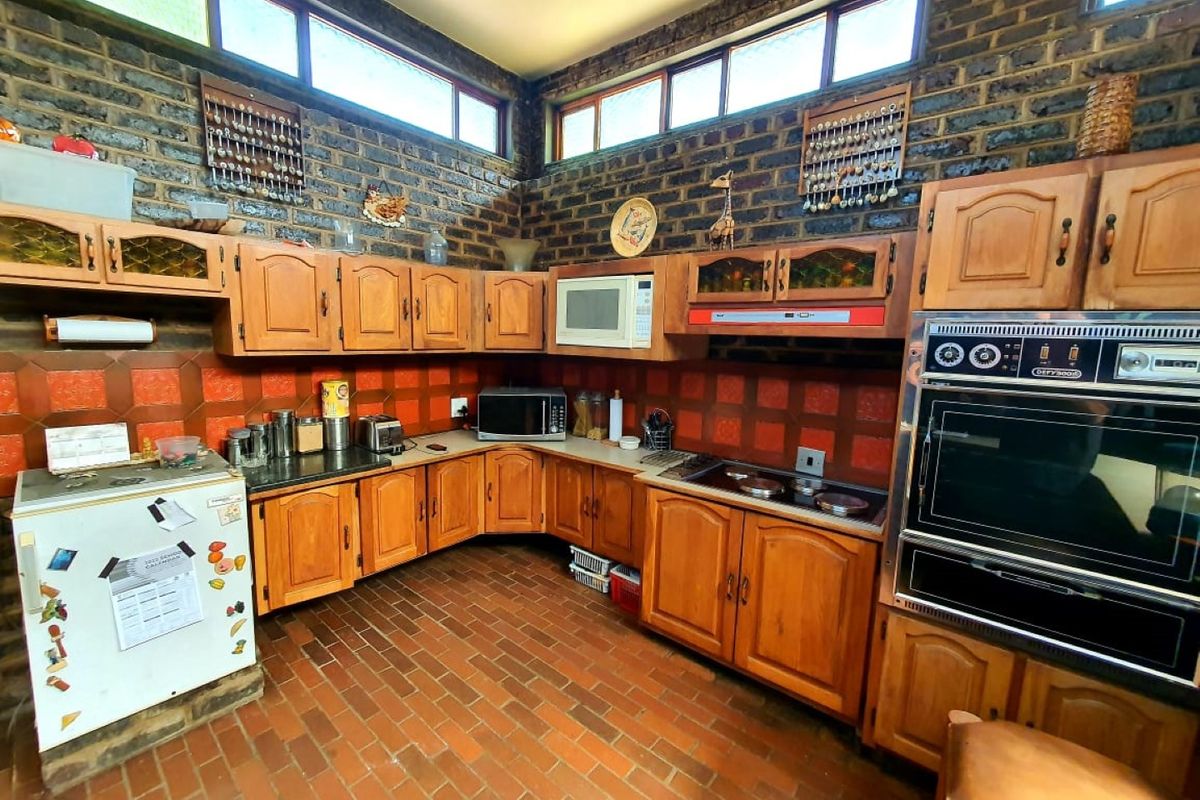 A rustic kitchen featuring timber cabinetry, built-in oven, electric hob, and distinctive brick walls with high-level clerestory windows providing natural light.