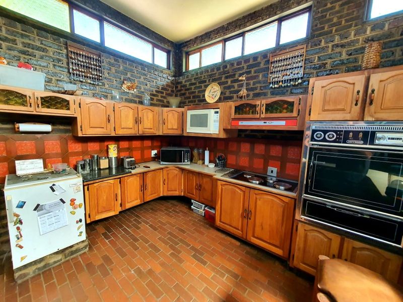A rustic kitchen featuring timber cabinetry, built-in oven, electric hob, and distinctive brick walls with high-level clerestory windows providing natural light.