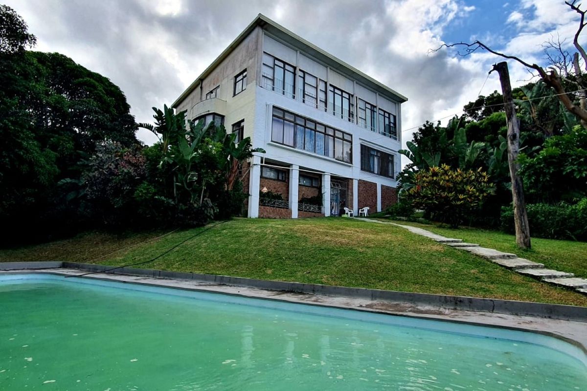 A multi-story residential building featuring a large swimming pool, stone masonry base, and expansive windows set within a landscaped garden.