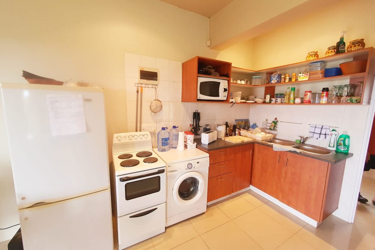 A functional kitchen featuring wood-look cabinetry, tiled flooring, a built-in sink, and space for a freestanding stove and washing machine.