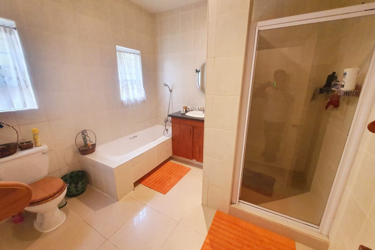 A functional bathroom featuring a built-in bathtub, separate glass-enclosed shower, vanity cabinet with basin, and tiled flooring throughout.
