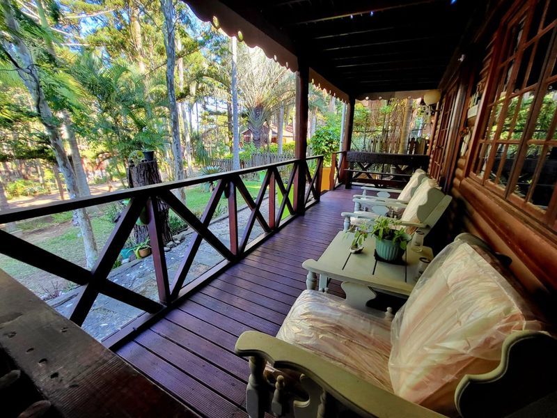 A covered timber balcony featuring wooden decking and balustrades, overlooking a lush garden area, providing a rustic outdoor living space.