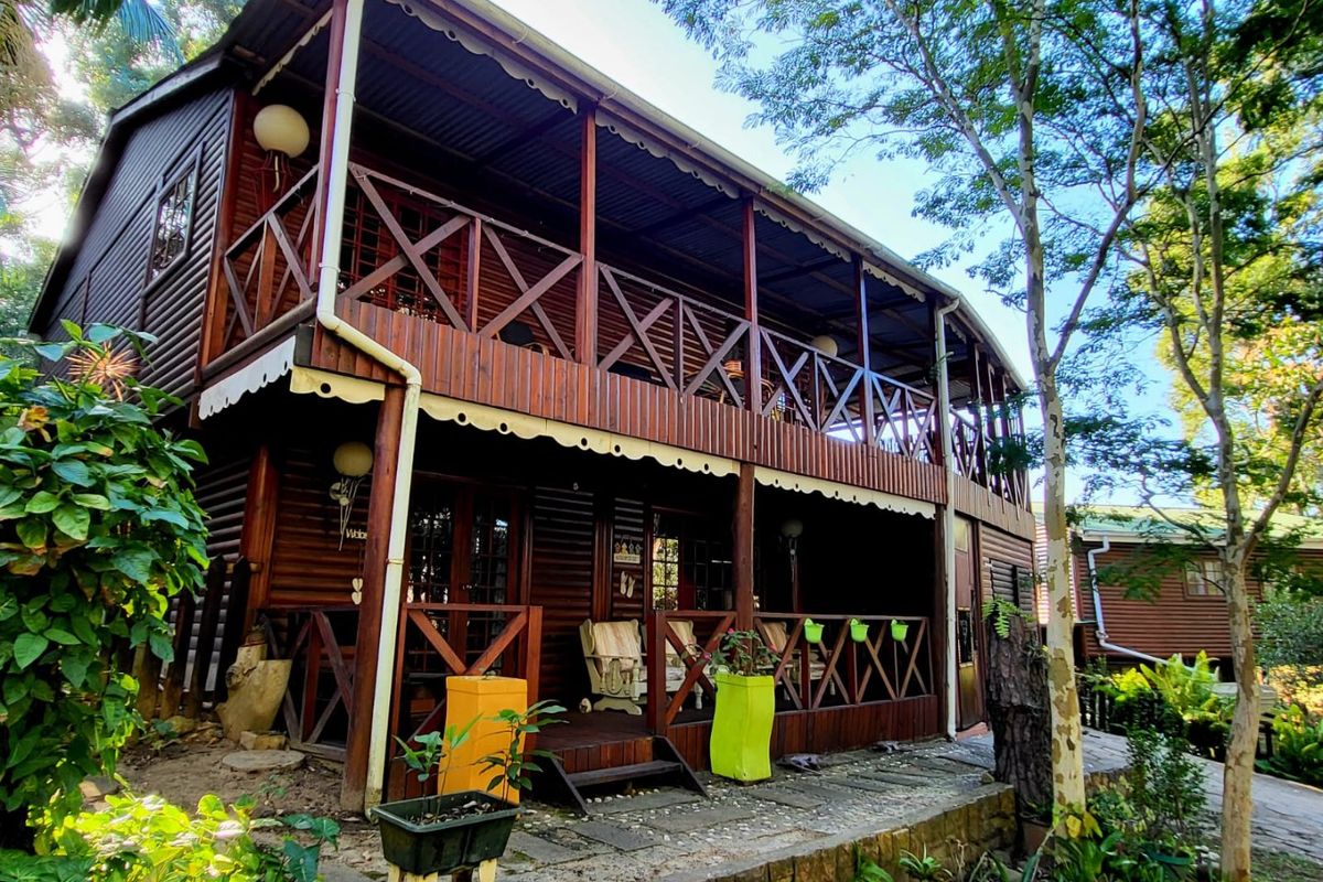 A two-storey timber townhouse featuring a wrap-around balcony with wooden balustrades and a ground-level paved patio area.
