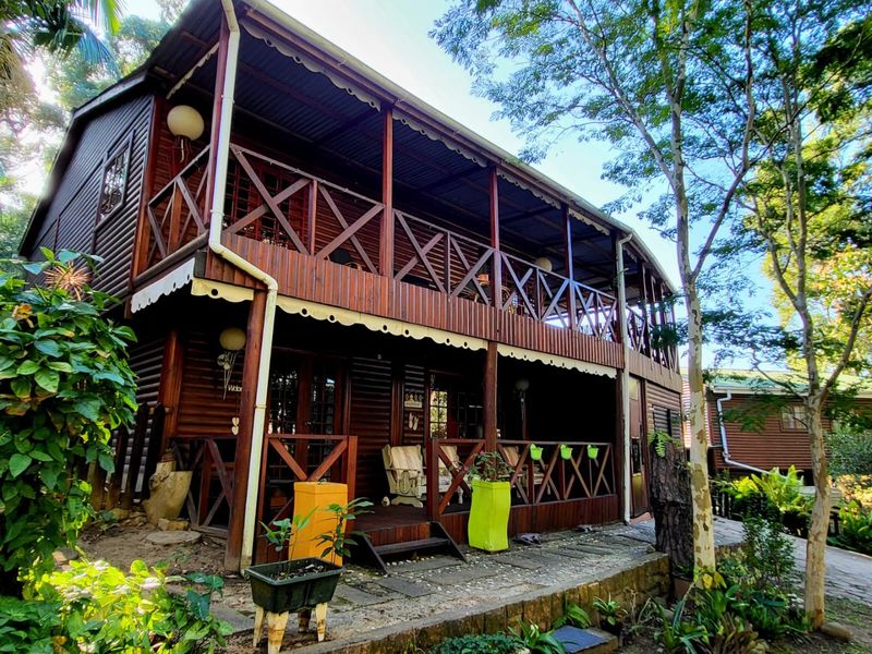 A two-storey timber townhouse featuring a wrap-around balcony with wooden balustrades and a ground-level paved patio area.