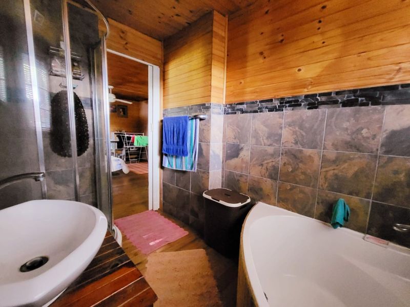 Bathroom featuring a corner bathtub, glass shower enclosure, vessel sink, and a combination of timber wall cladding and stone-look tiling.