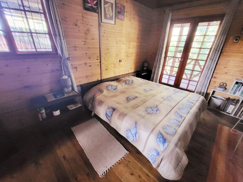 A cozy bedroom featuring natural timber wall cladding, wooden flooring, and timber-framed french doors providing access to the exterior.