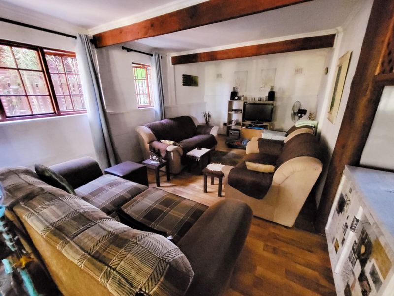 A cozy living room featuring exposed timber ceiling beams, laminate flooring, and large windows with security bars, offering a warm and traditional atmosphere.