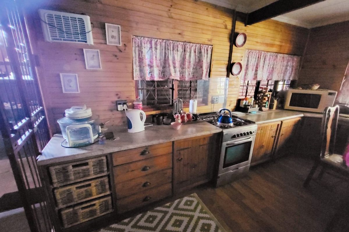 A rustic kitchen featuring timber wall cladding, built-in wooden cabinetry, laminate countertops, and a gas stove with oven.