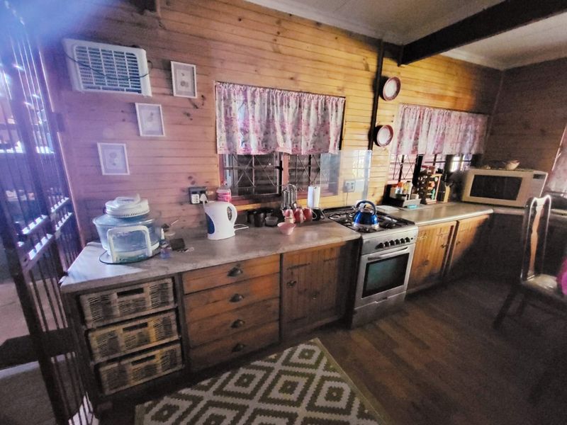 A rustic kitchen featuring timber wall cladding, built-in wooden cabinetry, laminate countertops, and a gas stove with oven.