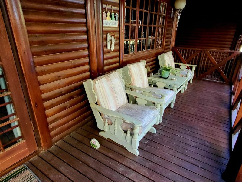 A covered timber patio featuring log wall construction, wooden decking, and a timber balustrade, providing a rustic outdoor living space.