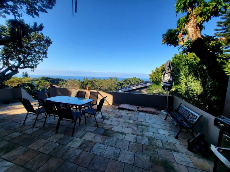 Spacious outdoor patio area featuring stone paving and a low perimeter wall, offering expansive elevated views of the surrounding landscape and ocean.