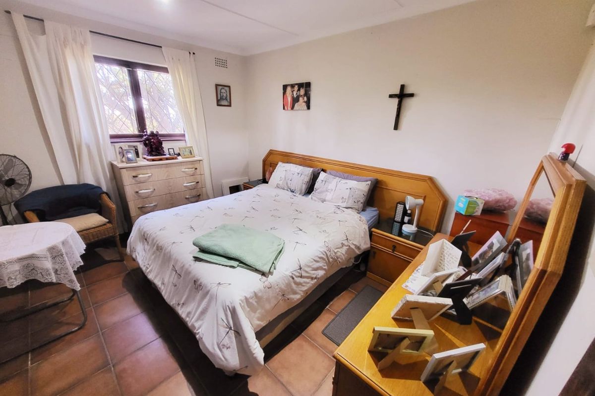 A bedroom featuring tiled flooring, a window with curtains, and a built-in headboard, offering a functional and comfortable living space.