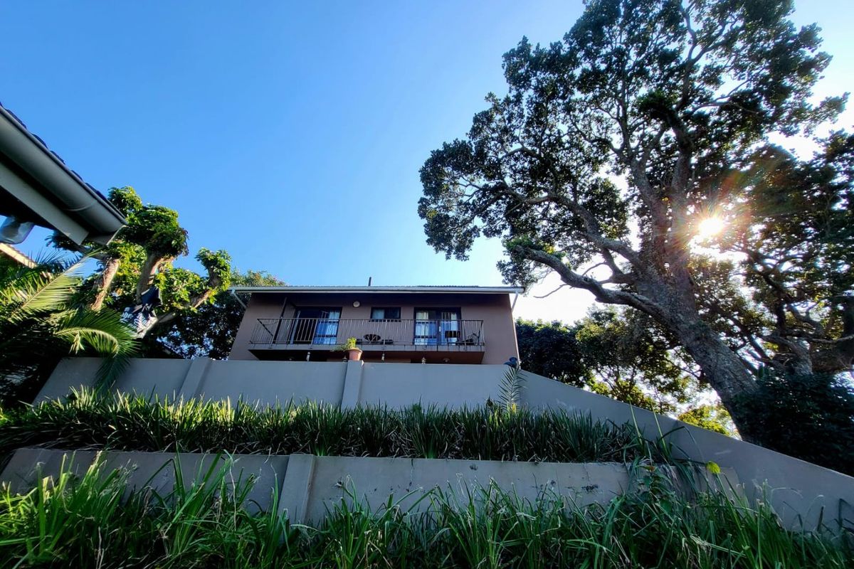 A low-angle view of the rear elevation of the house, featuring a balcony with metal railings and mature trees in the surrounding garden.