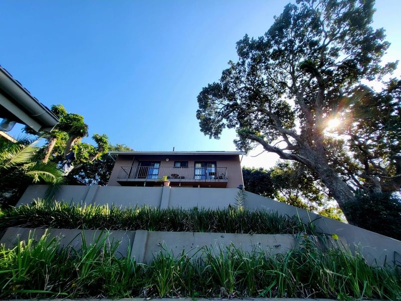 A low-angle view of the rear elevation of the house, featuring a balcony with metal railings and mature trees in the surrounding garden.