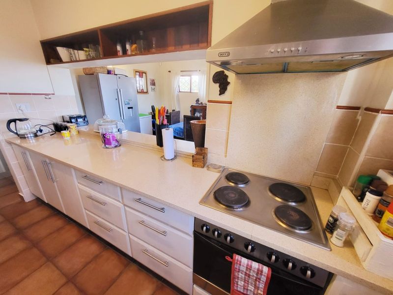 A functional kitchen featuring a built-in electric stove, stainless steel extractor fan, stone-look countertops, and ample cabinetry, with a convenient pass-through to the living area.